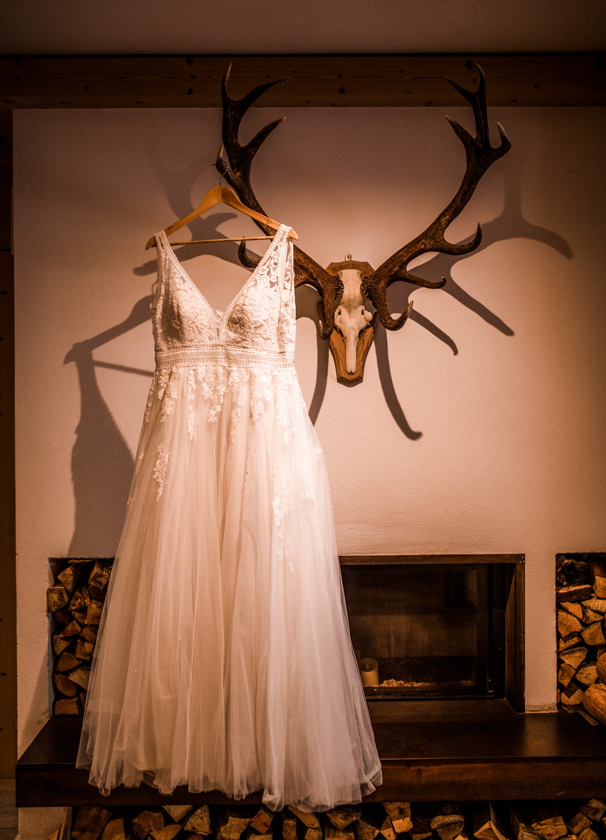 Brautkleid hängt an Hirschgeweih über dem Kamin einer Almhütte